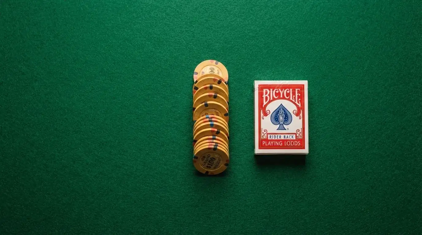 Vista cenital de fichas doradas y una baraja de cartas sobre una mesa de fieltro verde.