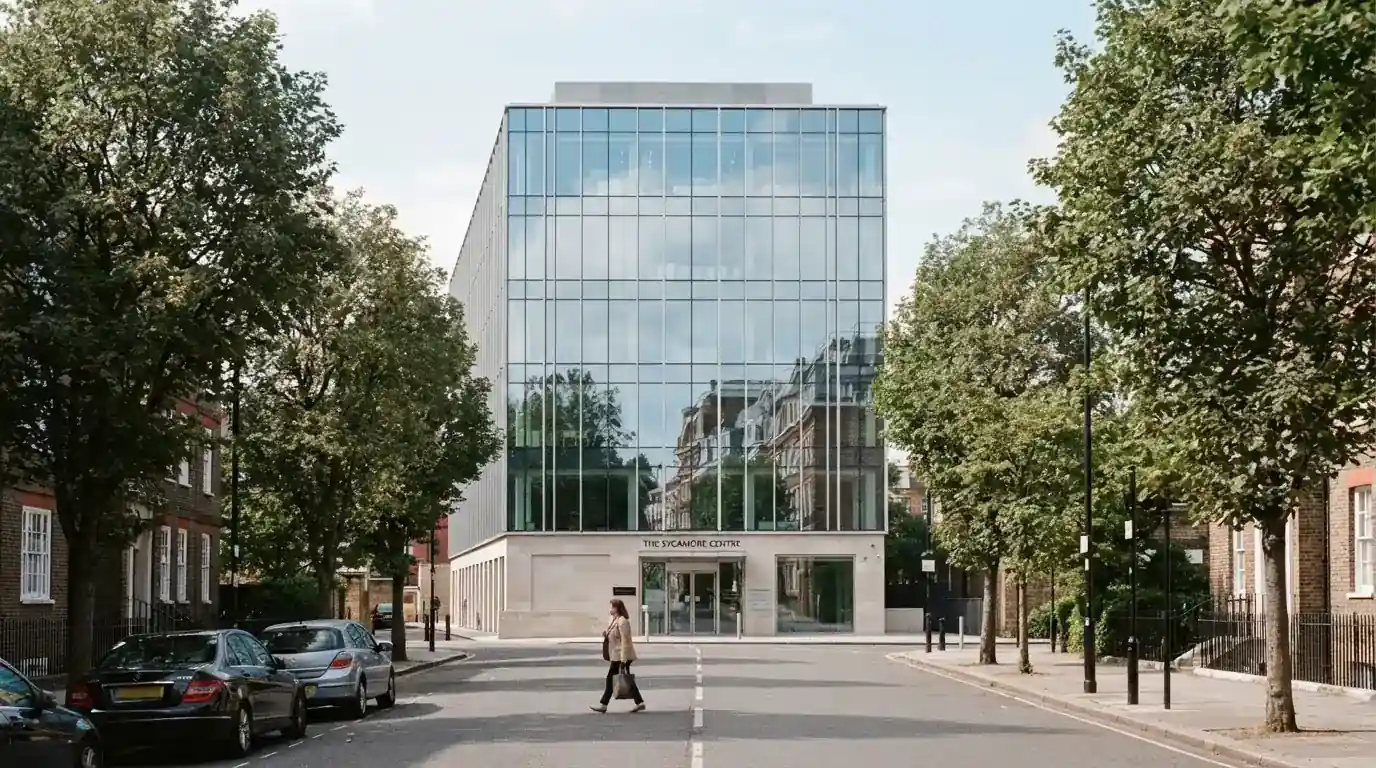 Un edificio de oficinas moderno con cristales reflectantes bajo un cielo despejado, visto desde una calle tranquila.