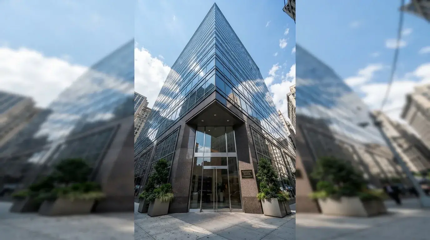 Un edificio de oficinas con fachada de cristal reflejando el cielo, fotografiado desde la acera de una calle ancha.